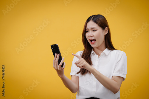 Woman reading good news on smartphone with excited face and enjoying isolated on yellow background