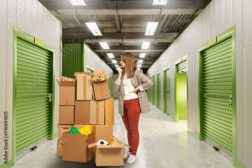 Woman chooses storage unit. Girl brought belongings to warehouse. Storage unit for temporary placement cargo. Woman in warehouse building. Corridor with closed storage units. Warehouse rental