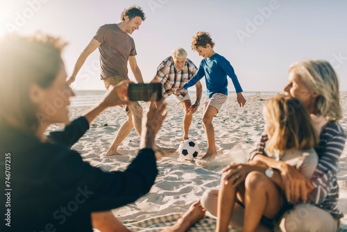 Family playing soccer on a sunny beach with kids and grandparents photo