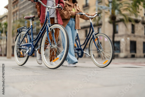 Cropped picture of friends walking on the street and pushing bicycles.