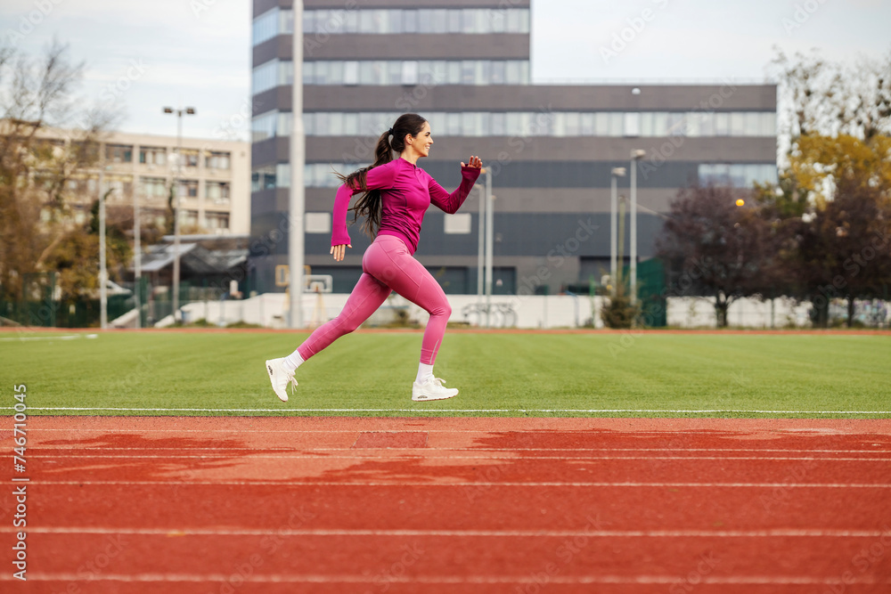 A fast female athlete in shape is jumping and running at stadium.