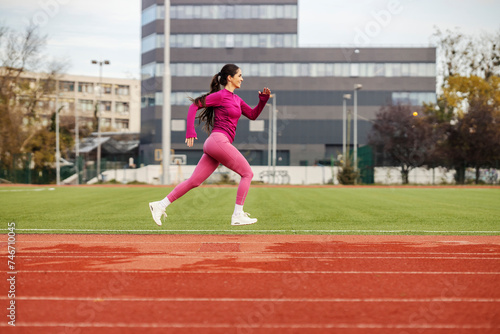 A fast female athlete in shape is jumping and running at stadium.
