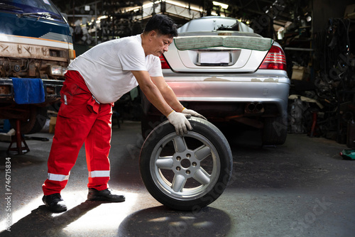 mechanic holding and pushing a tire for fixing in garage © offsuperphoto