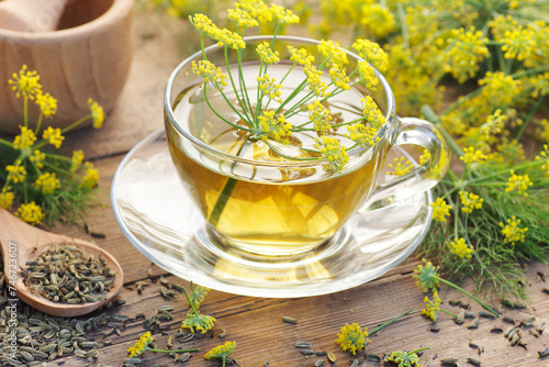 Quadro em tela Fennel seed tea or extract on wooden background with fresh flowers nearby, copy