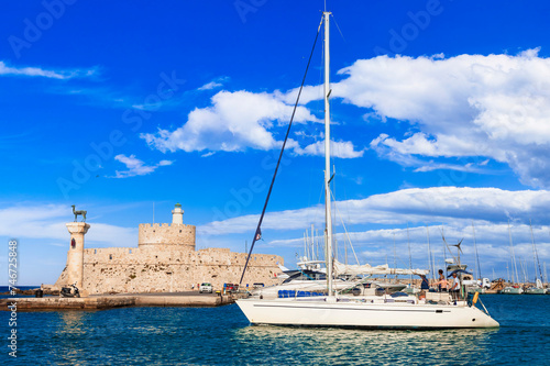 Greece travel, Dodecanese. Rhodes island. Mandraki Harbor with symbol statue of deer , saillboats and old lighhouse