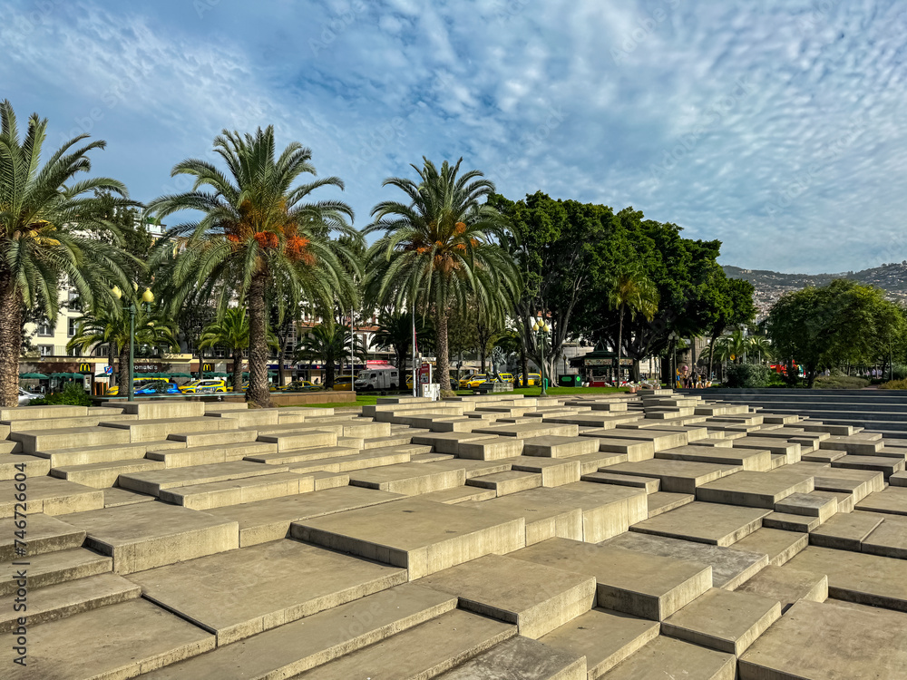 Fototapeta premium Artistic monument made of stone steps in the park and promenade at the harbor in Funchal, Madeira island, Portugal, Europe. Steps made of concrete and there are palm trees on either side of the square