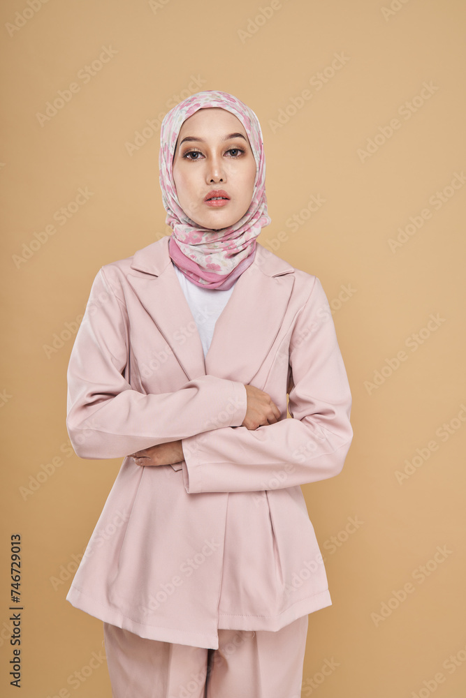 Fototapeta premium Portrait of a beautiful Muslim female model wearing stylish pink office attire with hijab isolated over beige studio background. Fashion, beauty, style concept.