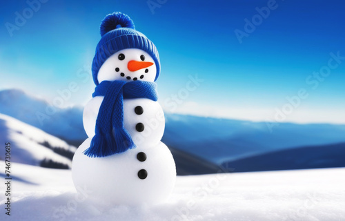 Little snowman in a blue knitted hat and scarf in winter on the snow against the backdrop of mountains on a sunny frosty day © isavira