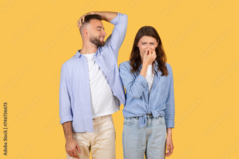 Man sniffs armpit and smiling, woman covers nose Man sniffs armpit and smiling, woman covers nose