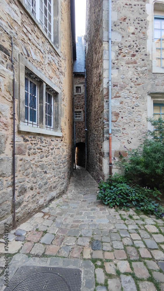 Vertical photo of the picturesque very narrow alley of the old town of Le Mans in France, old style inner courtyard, stone houses