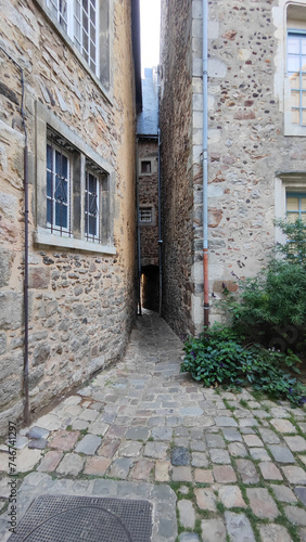 Vertical photo of the picturesque very narrow alley of the old town of Le Mans in France, old style inner courtyard, stone houses
