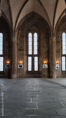 Large hall on Mont Saint Michel in France, near the church with spectacular columns and medieval architecture windows. There are paintings as an exhibition