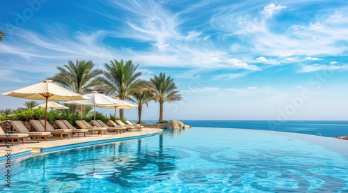 Luxurious swimming pool and loungers umbrellas near beach and sea with palm trees.
