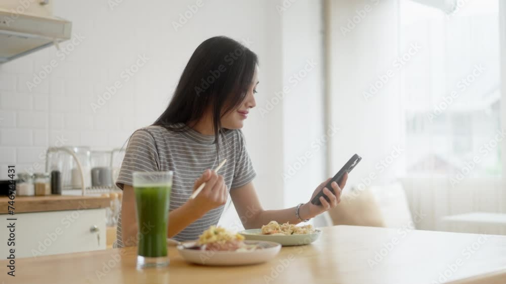 Young asian woman using smartphone while eating on counter table Young asian woman using smartphone while eating on counter table