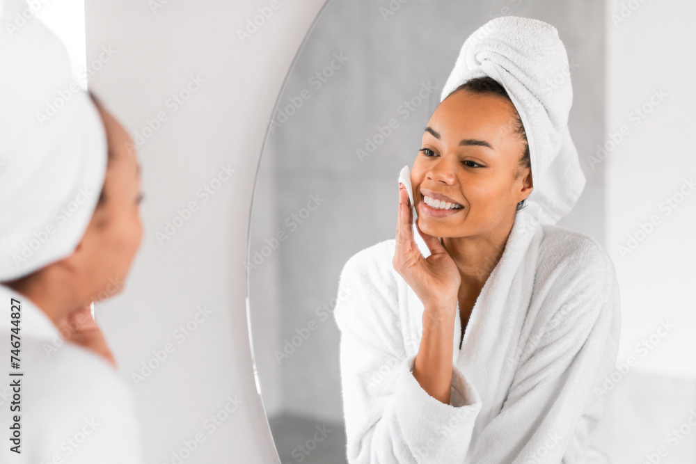 Black millennial woman applying micellar water with cotton pad indoors Black millennial woman applying micellar water with cotton pad indoors