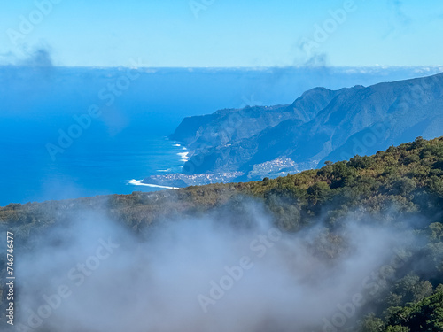 Panoramic view of majestic coastline of Atlantic Ocean seen from mountain top of Fanal, Madeira island, Portugal, Europe. Clouds coming up from sea. Tranquil serene atmosphere on sunny summer day