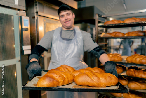 close up In a professional kitchen an inclusive baker stands with ready-made bread on a tray smiling