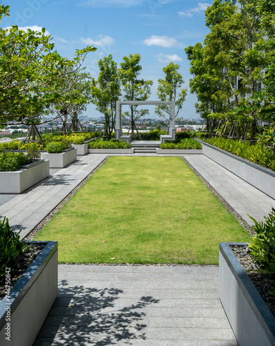 A neatly manicured rooftop garden pathway leading to a modern pergola with a panoramic city view.