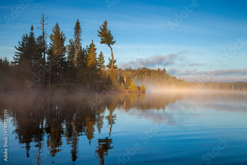Blue trout lake and island in northern Minnesota with fog on the water at sunrise during September
