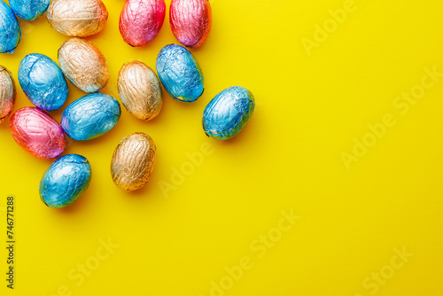 Easter chocolate eggs wrapped in aluminium foil on yellow background. Top view.