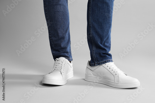 Man wearing stylish white sneakers on grey background, closeup
