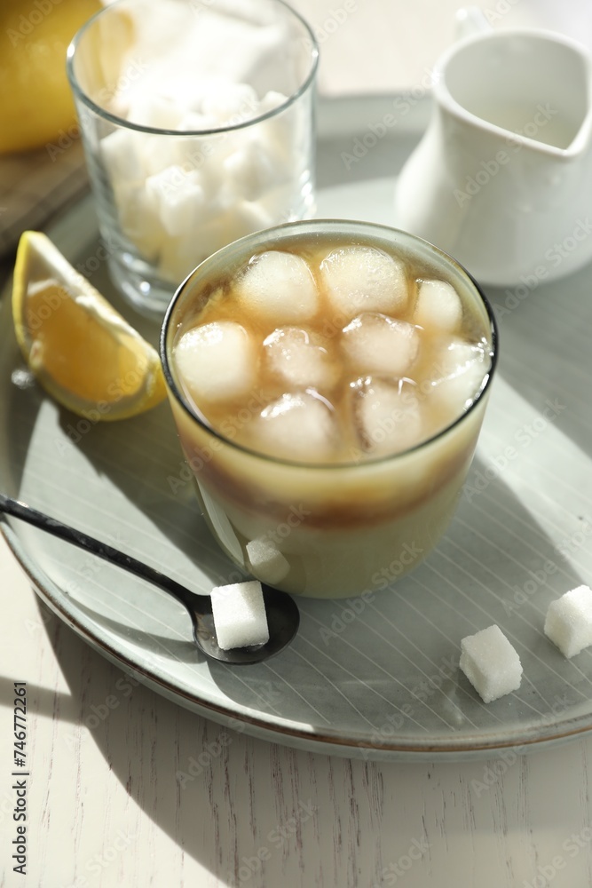 Refreshing iced coffee with milk in glass, sugar cubes and spoon on white wooden table Refreshing iced coffee with milk in glass, sugar cubes and spoon on white wooden table