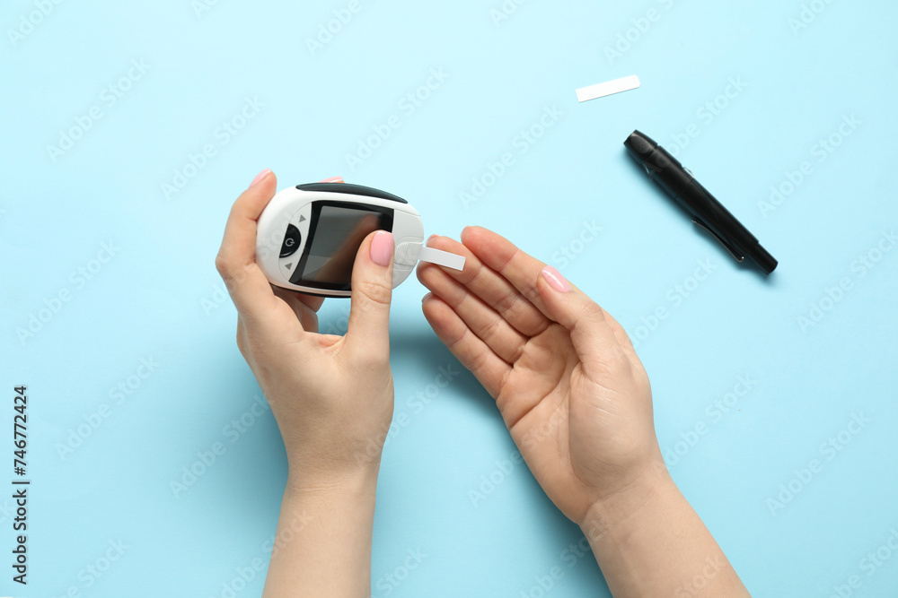 Diabetes. Woman checking blood sugar level with glucometer on light blue background, top view