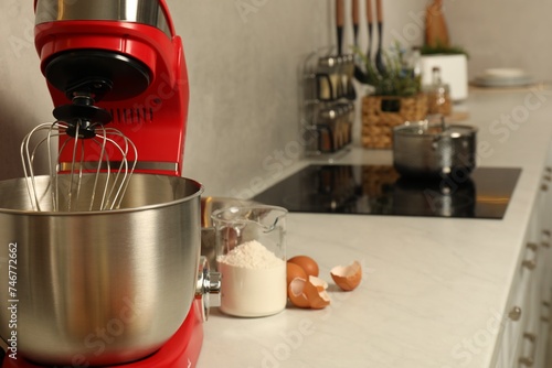 Modern red stand mixer, eggs and container with flour on white marble countertop in kitchen. Space for text