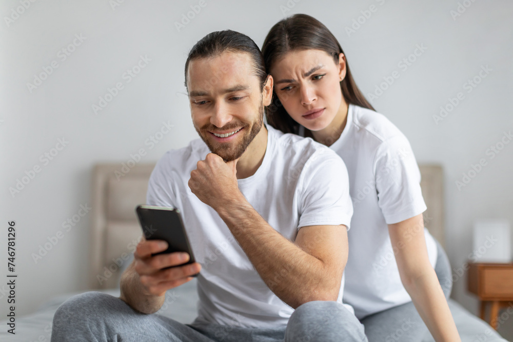 Worried woman peering over man's shoulder at phone Worried woman peering over man's shoulder at phone
