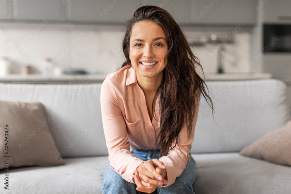 Confident woman smiling, sitting casually on grey couch Confident woman smiling, sitting casually on grey couch