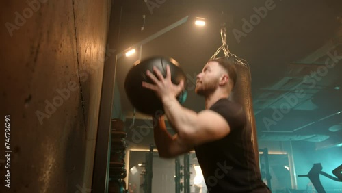 Engaging in a high-intensity workout, a man performs squats combined with the explosive action of throwing a medicine ball against a wall, maximizing his fitness routine. Camera 8K RAW. 