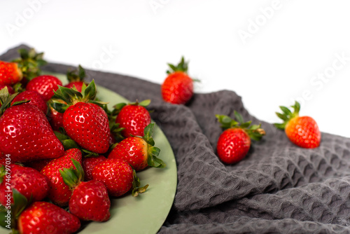 Red strawberries on a gray towel and a light green plate on a white background.