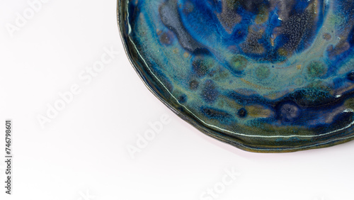 Fragment of a ceramic plate with stains of blue and green glaze on a white background.