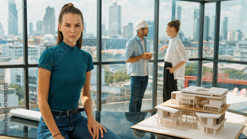 Young beautiful interior designer looking at camera while engineer team talking about house design. Skilled businesswoman smiling at camera with confident while sitting near house model. Tracery