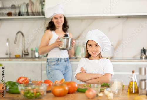 Girl poses against background of kitchen interior. Small scullion with ladle stands in kitchen after cooking