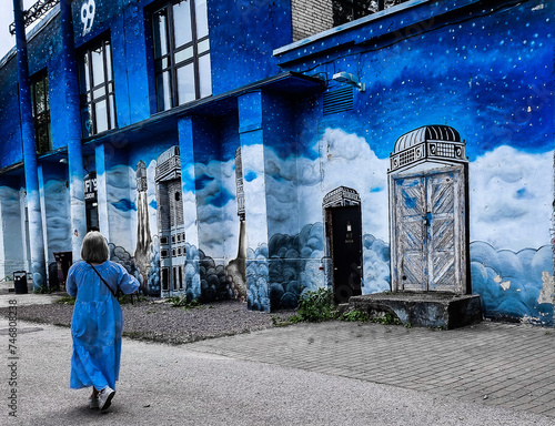 A lady in blue gown walking through the streets of Tallinn in Estonia with a background of blue wall art building.