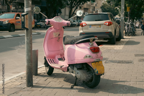 Pink scooter parked on a sunny street in Tel Aviv, Israel, with cars and bicycles in the background.