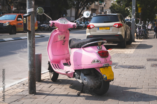 Pink scooter parked on a sunny street in Tel Aviv  Israel  with cars and bicycles in the background.