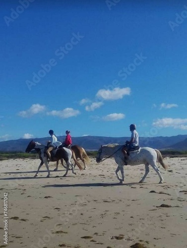 Personas montando a caballo en la playa.