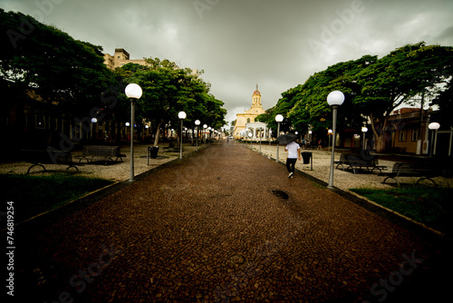 Praça da cidade de Itu com igreja matriz de cor amarela, ruas, árvore, poste de rua com luz acesa e céu com nuvens carregadas.  © Luiz