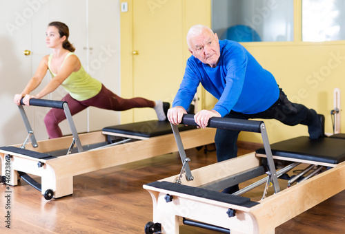 Elderly man press exercises on pilates reformer at studio. Front view