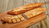 Chopped loaves of freshly baked french baguette bread on wooden table..