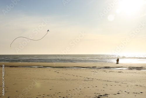 Dad and teenagers flying kites together on the beach at sunset.  Stunt kit with beautiful sky and ocean in the background.