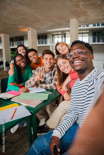 Happy young students taking a vertical selfie portrait together at university library. African american guy shooting a photo with his smiley classmates on a high school meeting. Friends at academy