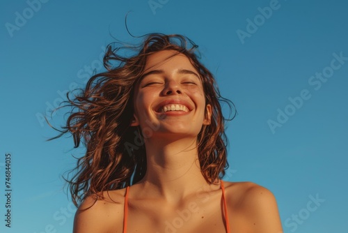 Fit woman smiling deep breathing in front of clear blue sky on a windy summer day © VolumeThings