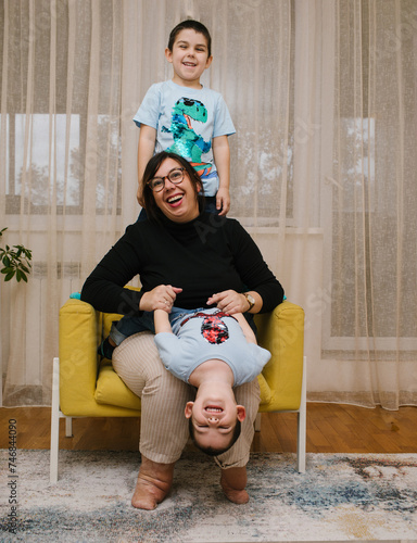 Mother with disability playing with her children.  
Young mother with a disability having fun with her little children at home. 