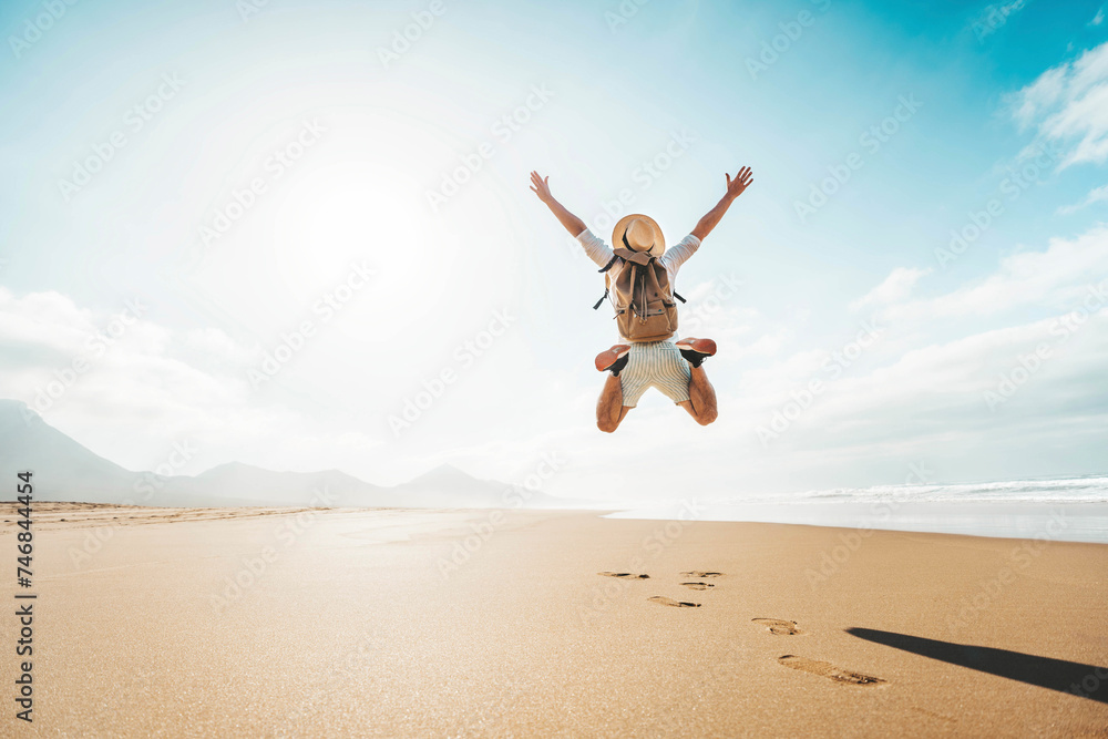Happy traveler with hands up jumping at the beach - Delightful man enjoying success and freedom outdoors - Wanderlust, wellbeing, travel and summertime holidays concept - obrazy, fototapety, plakaty 