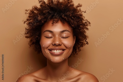 Joyful African American woman with curly hair delighting in her refreshed skin after a spa treatment against a brown backdrop with her eyes closed in happines