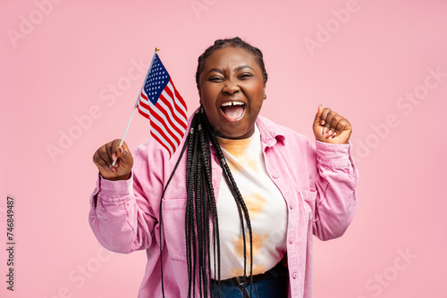 Fotografie Portrait happy stylish African American woman, supporter holding USA flag, waiting for presidential election result isolated on pink background