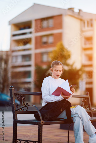 Blonde Teenager Engrossed in a Book at the Park Bench